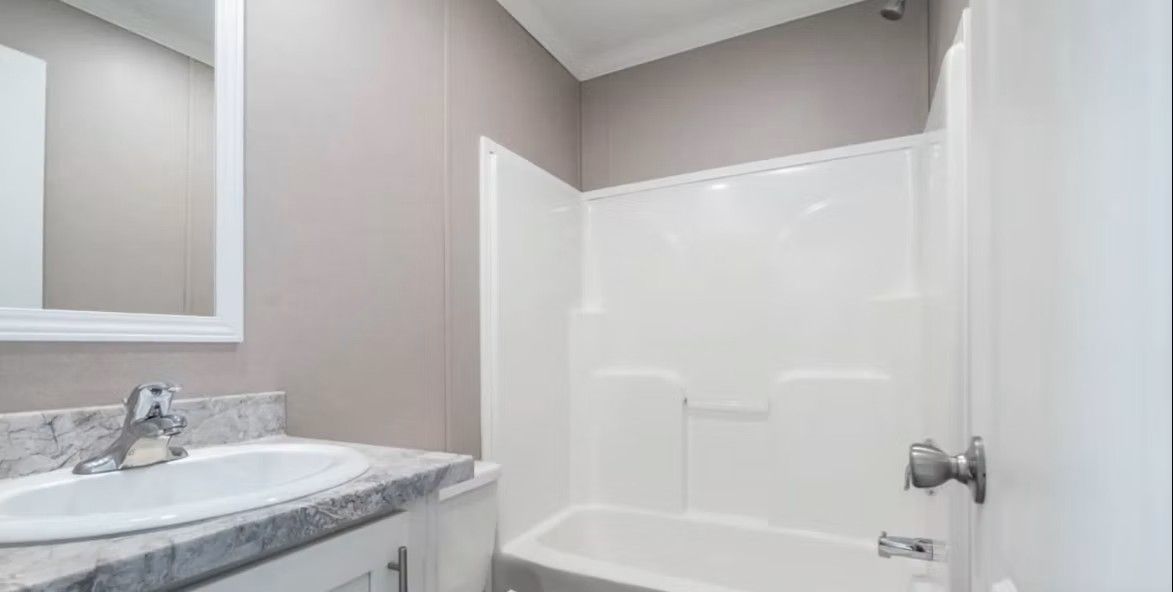 Bathroom with white tub/shower, sink, and mirror. Gray walls and white cabinet.
