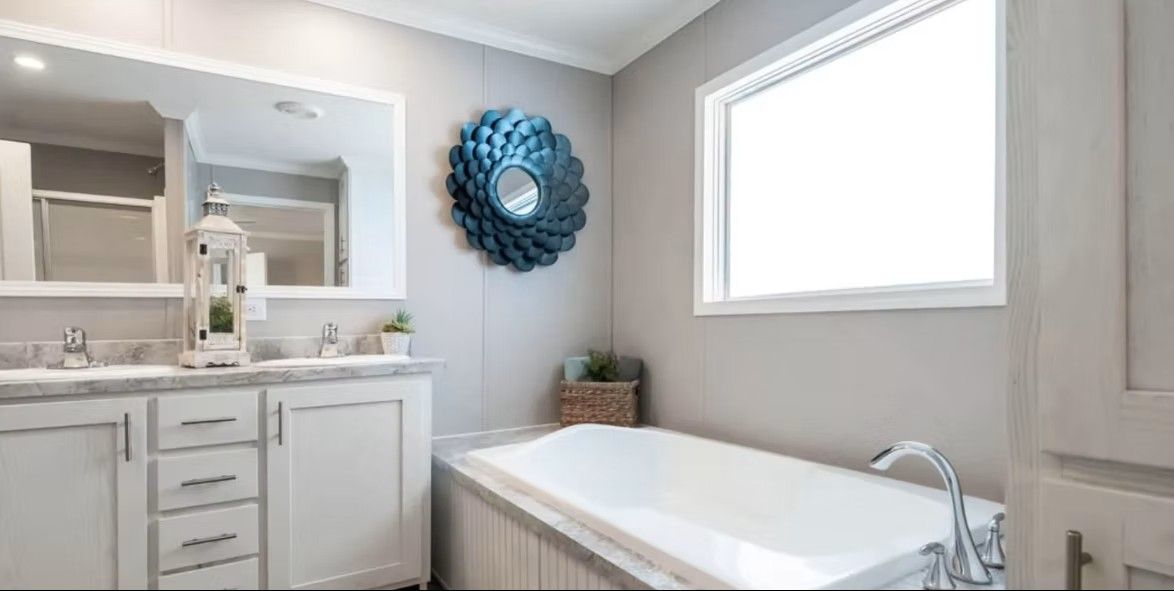 Bathroom with a white bathtub, vanity, and a large mirror. A blue decorative mirror hangs on the wall.