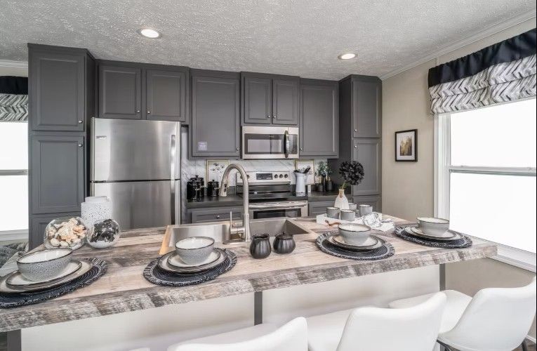 Modern kitchen with gray cabinets, stainless steel appliances, and a wooden island with white barstools.
