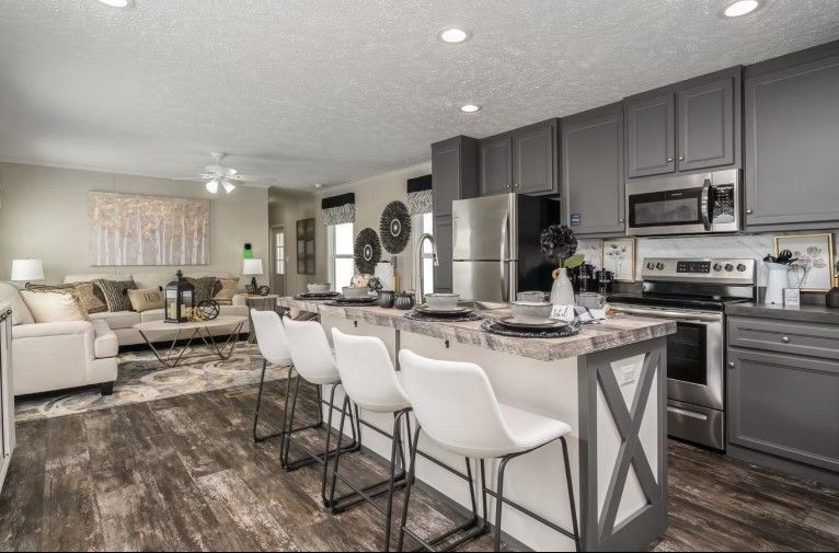 Kitchen and living room with gray cabinets, stainless steel appliances, and a breakfast bar with white chairs.