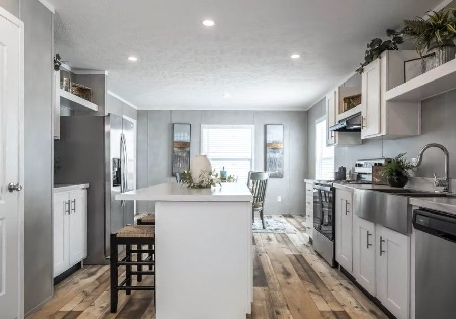 Modern kitchen with white cabinets, stainless steel appliances, island, and wood floors.