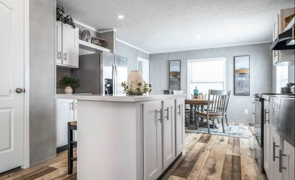 Kitchen with white cabinets, island, and wood floors, leading to dining area with table and chairs.