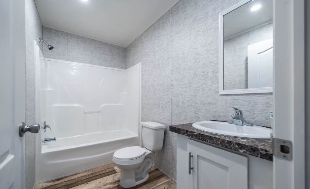Bathroom with white fixtures, vanity, toilet, and a bathtub with shower. Light gray walls.