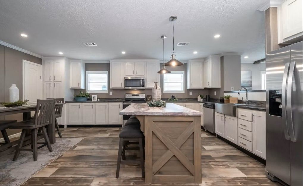 Spacious kitchen with a large island and stainless steel appliances.  Wooden floors, white cabinets, and farmhouse style.