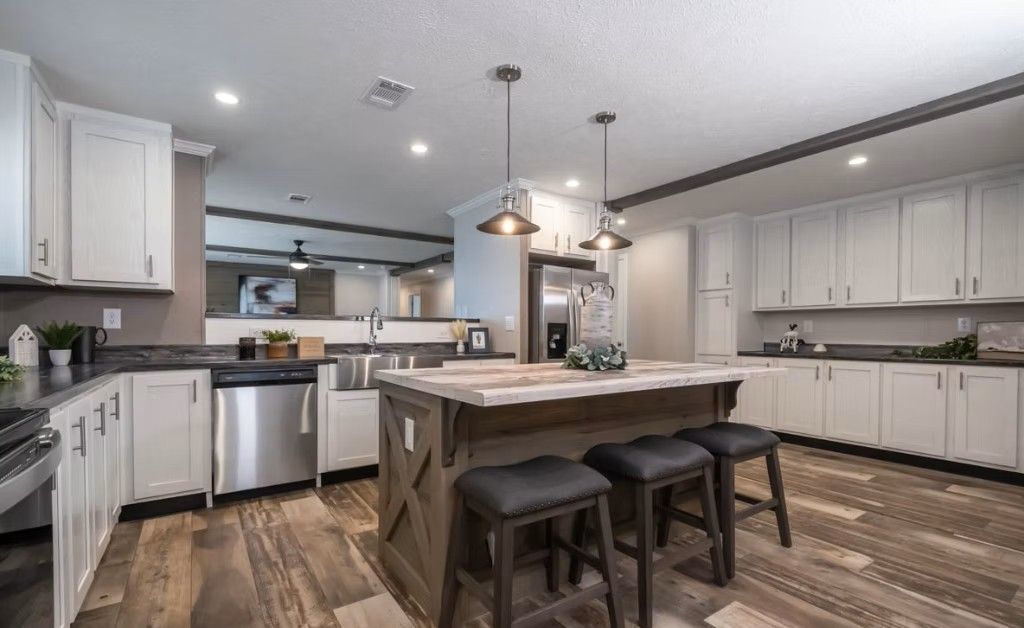 Kitchen with white cabinets, wood island with stools, stainless steel appliances, and wood-look flooring.