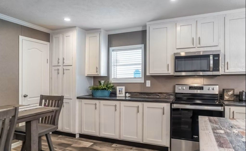 White kitchen with cabinets, microwave, and stove. Window with blinds, a table with chairs.