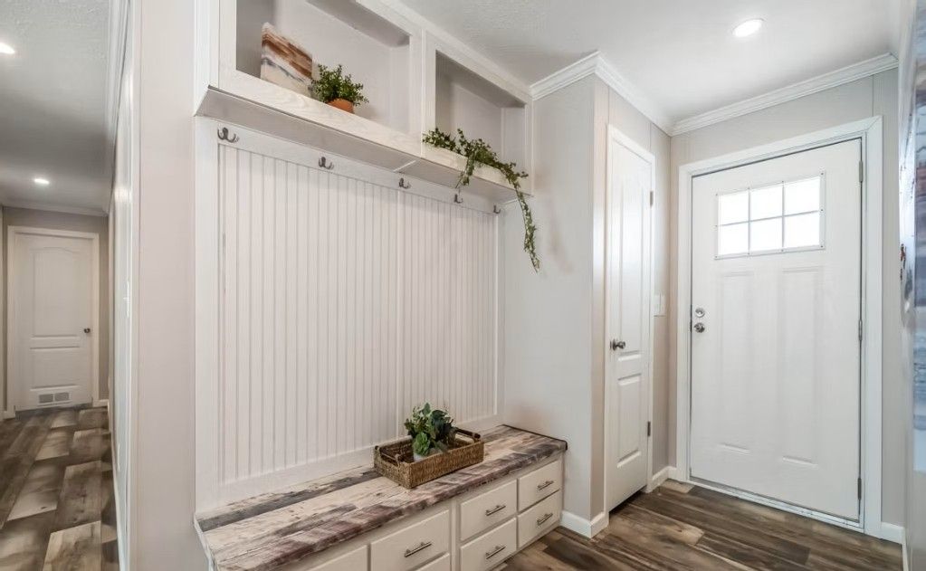 Entryway with white door, built-in bench, storage, and shelf; neutral color scheme.