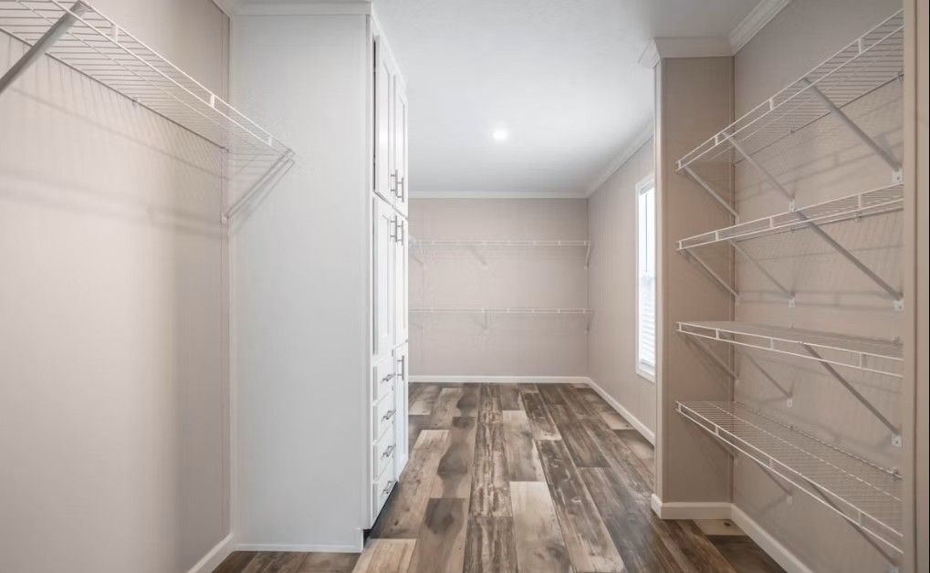 Walk-in closet with wire shelving and a tall cabinet, featuring wood-look flooring and beige walls.