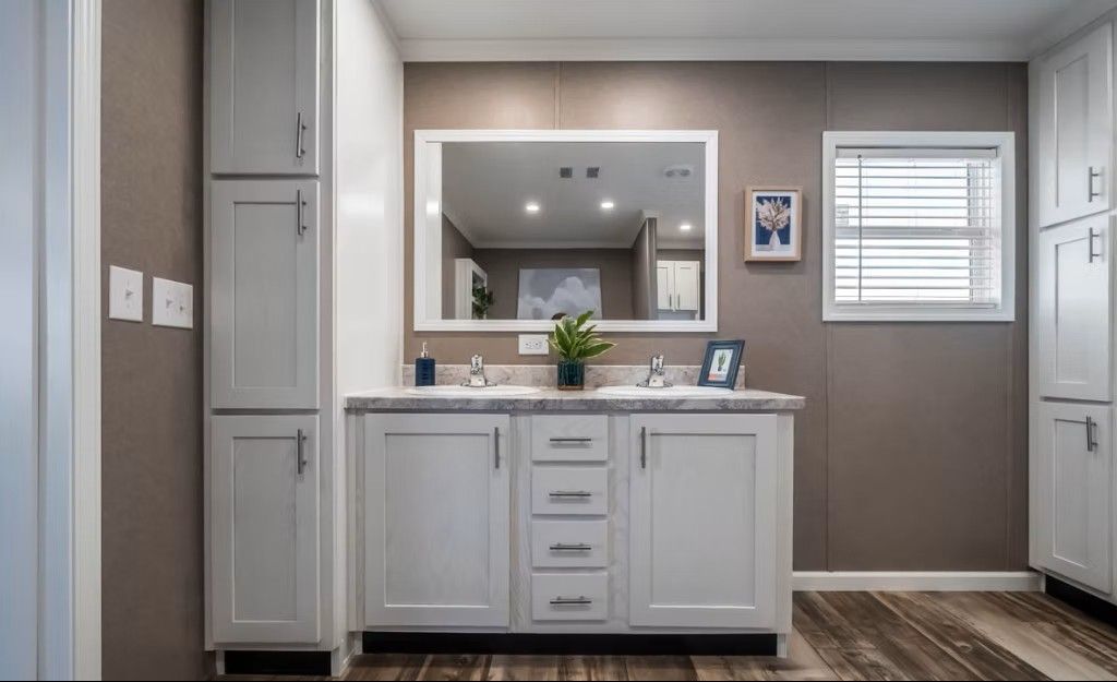 Bathroom with white cabinets, double sink, large mirror, and brown walls.