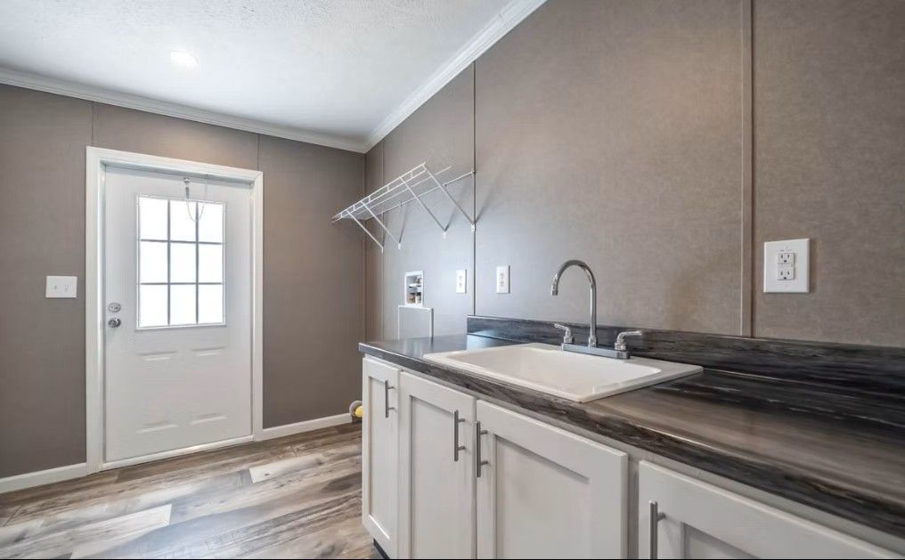 Laundry room with white cabinets, a sink, and a drying rack on a gray wall.