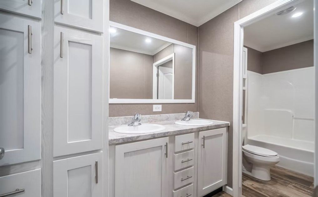 Bathroom with white cabinets, double sink, and a walk-in shower.