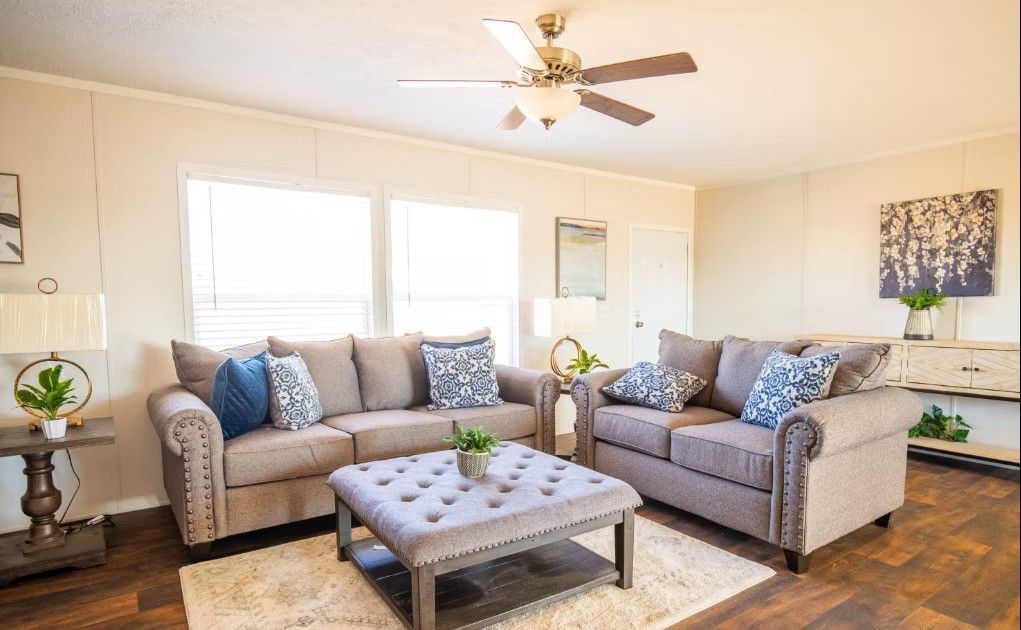 Living room with gray sofas, a tufted ottoman, and a ceiling fan.