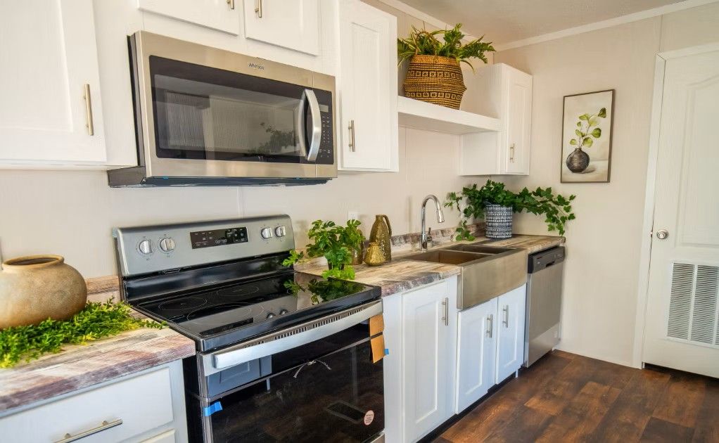 White kitchen with stainless steel appliances, plants, and a farmhouse sink.