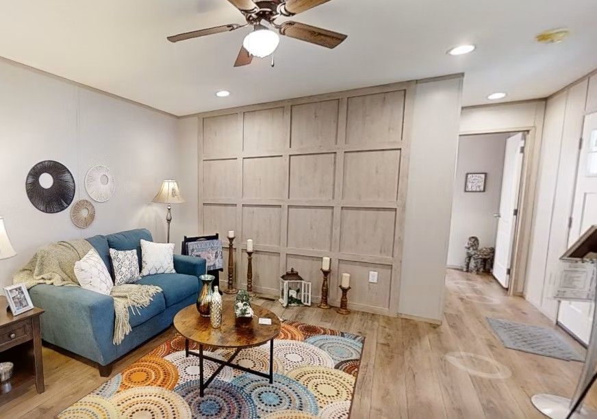 Living room with blue sofa, patterned rug, wooden panel wall, and open doorway.