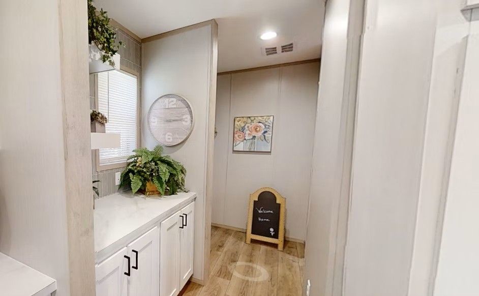 Narrow hallway with white cabinets, wood floors, and decorative wall art.