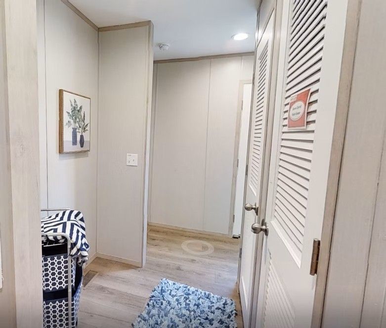 Hallway with closed white louvered door, neutral walls, framed art, and patterned rug.