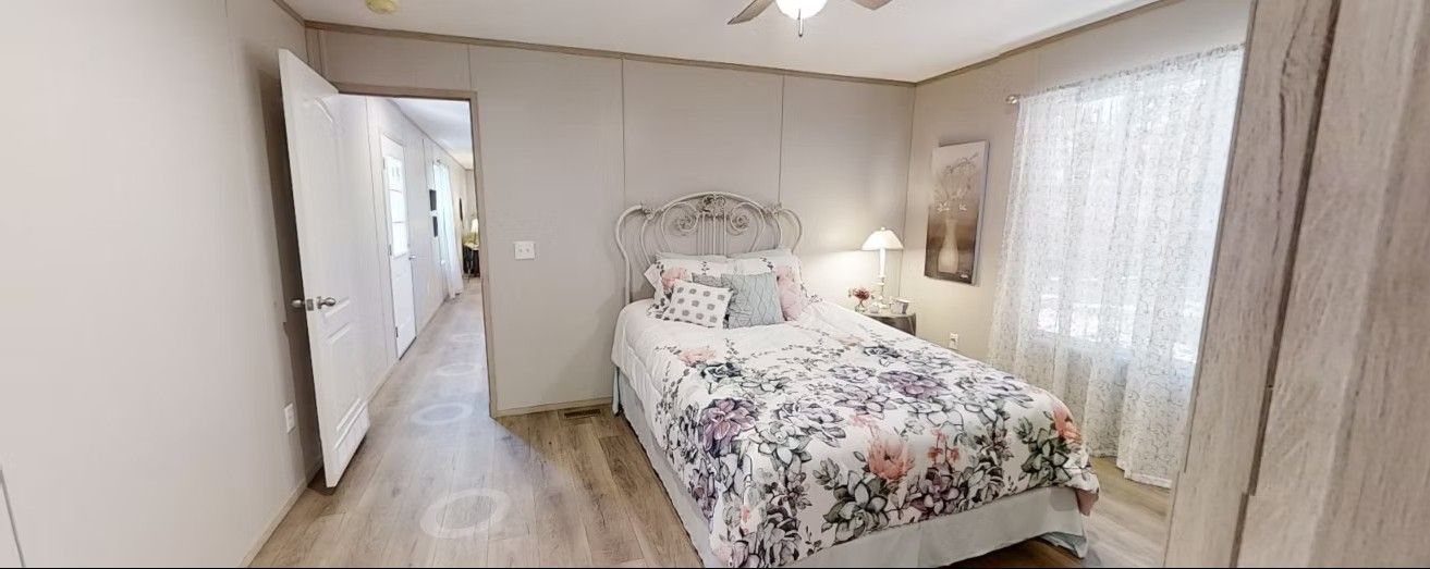 Bedroom with bed, floral bedding, window with curtains, and open door to a hallway.