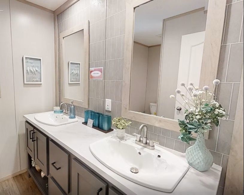 Bathroom with two sinks, gray tile, large mirrors, white countertop, and gray cabinets.