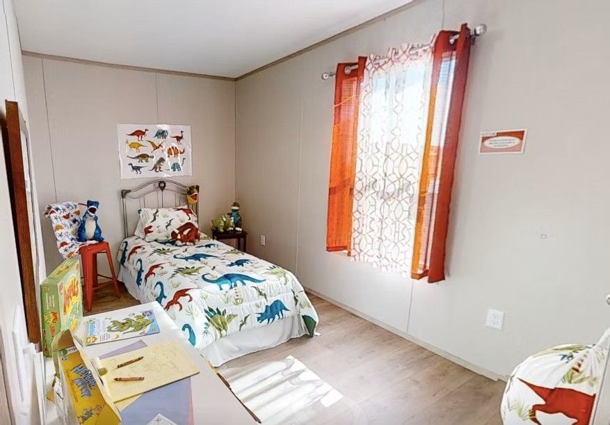 Dinosaur-themed bedroom with bed, desk, and window with orange curtains.