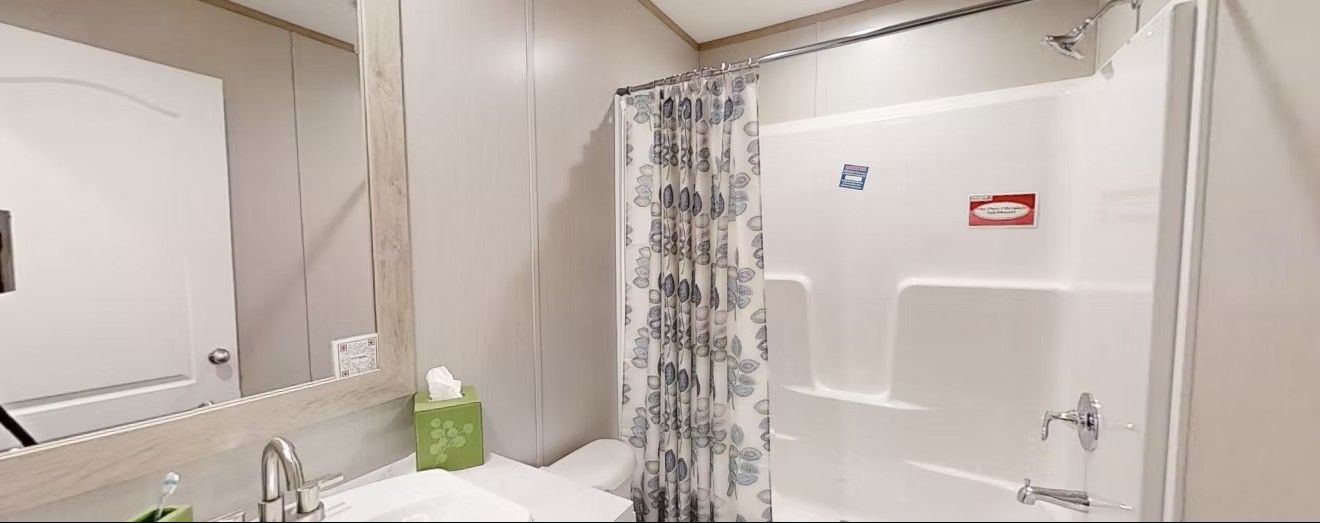 Bathroom with a white sink, mirror, shower, and toilet. A patterned shower curtain is visible.