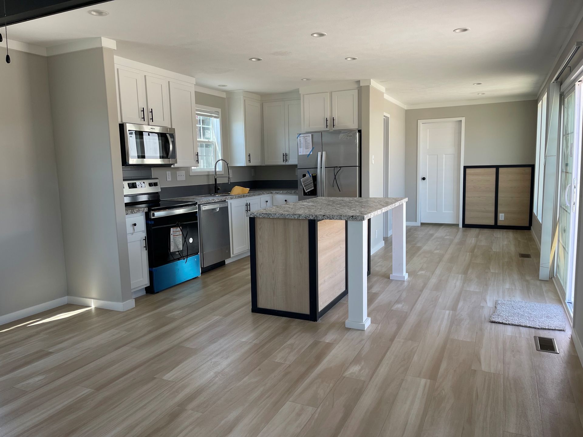 Empty modern kitchen and living area with light wood floors, white cabinets, and an island.
