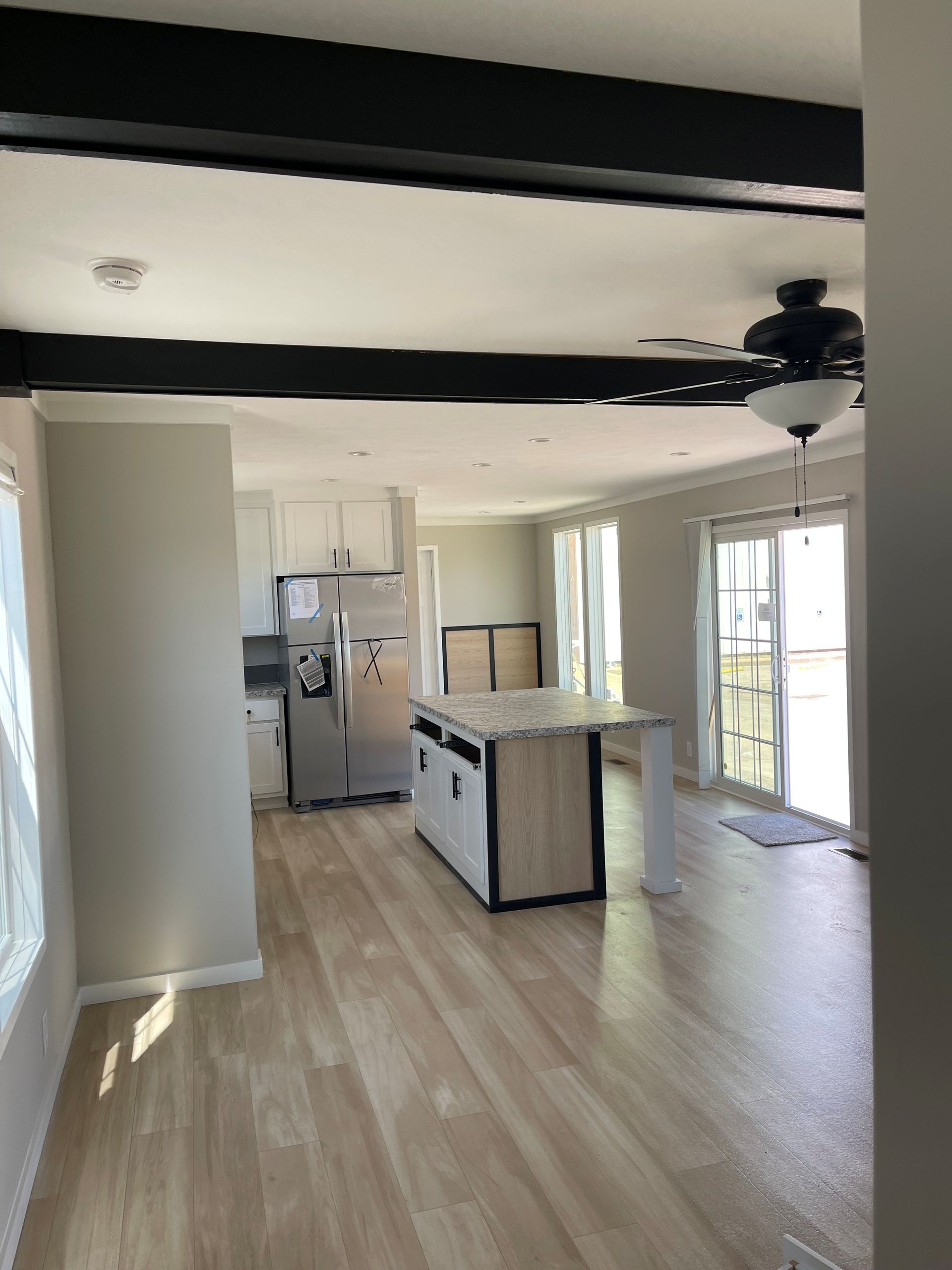 Damaged kitchen interior with exposed black ceiling beams and an island on light wood flooring.