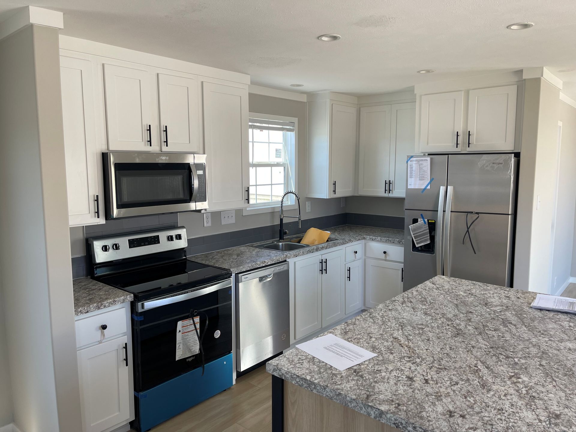 Bright kitchen with white cabinets, stainless appliances, and a granite countertop island.