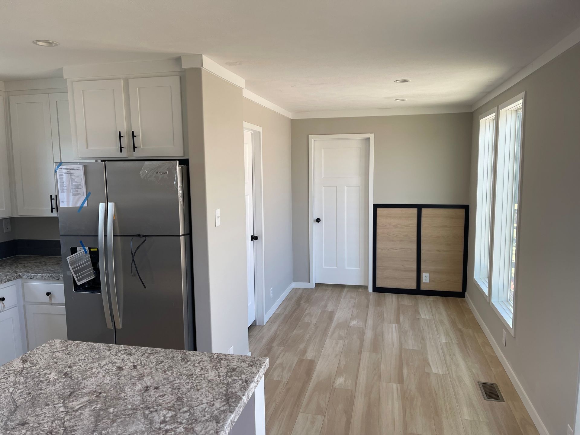 Bright kitchen and hallway with stainless steel fridge, white cabinets, and wood flooring.