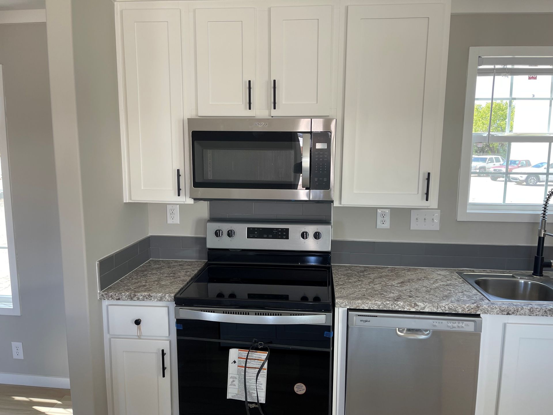 White kitchen with stainless steel stove, microwave, and dishwasher beneath gray granite countertops.