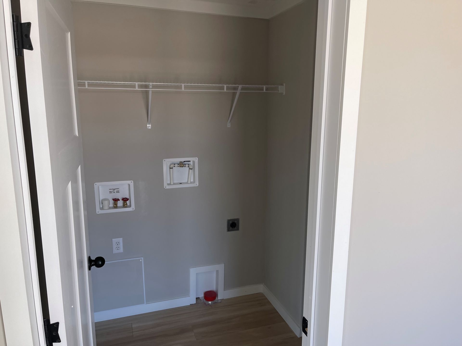 Empty beige laundry closet with wire shelf, wall hookups, and light wood floor