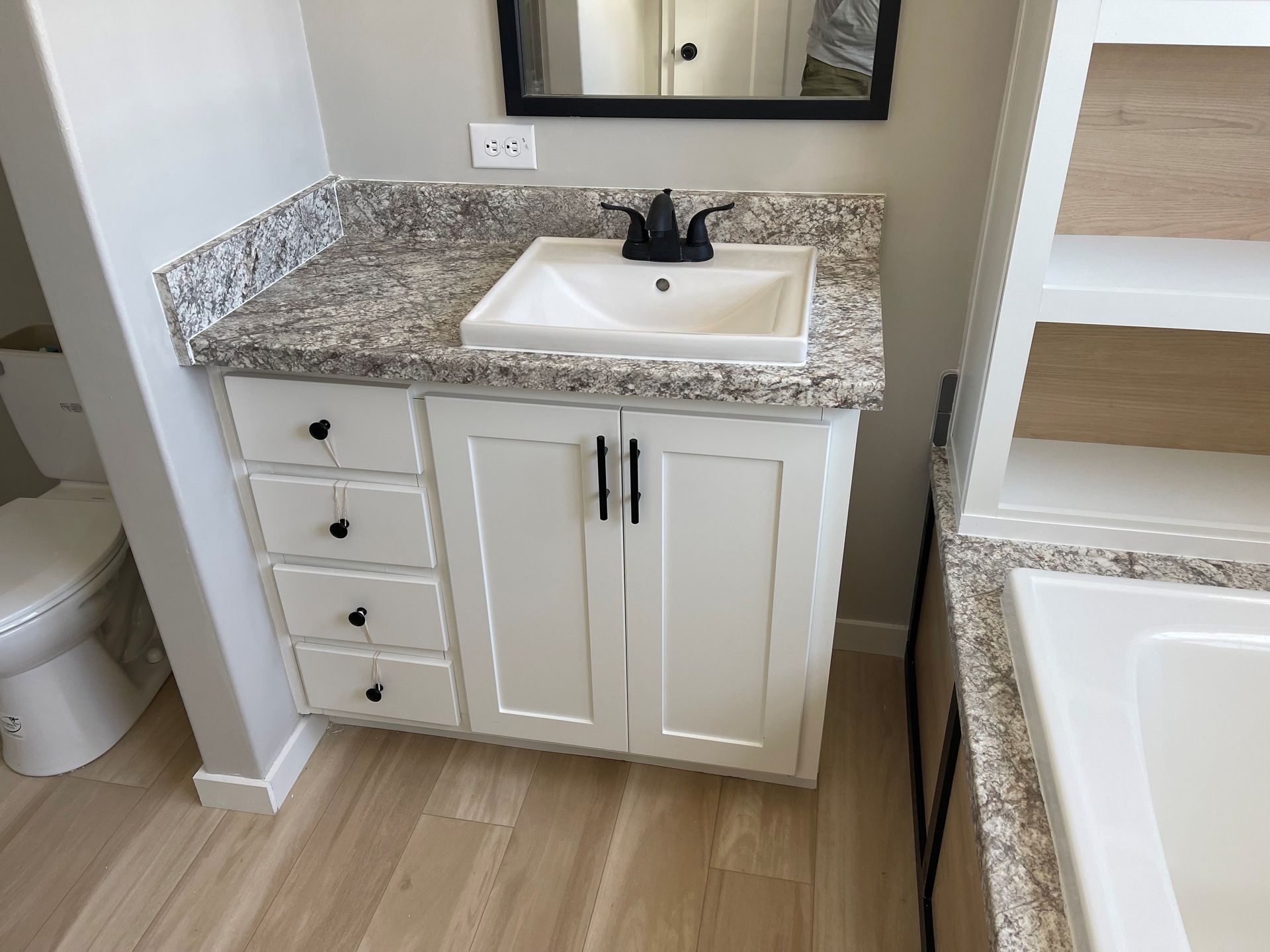 Bathroom vanity with white cabinet, granite countertop, sink, mirror, and adjacent bathtub edge