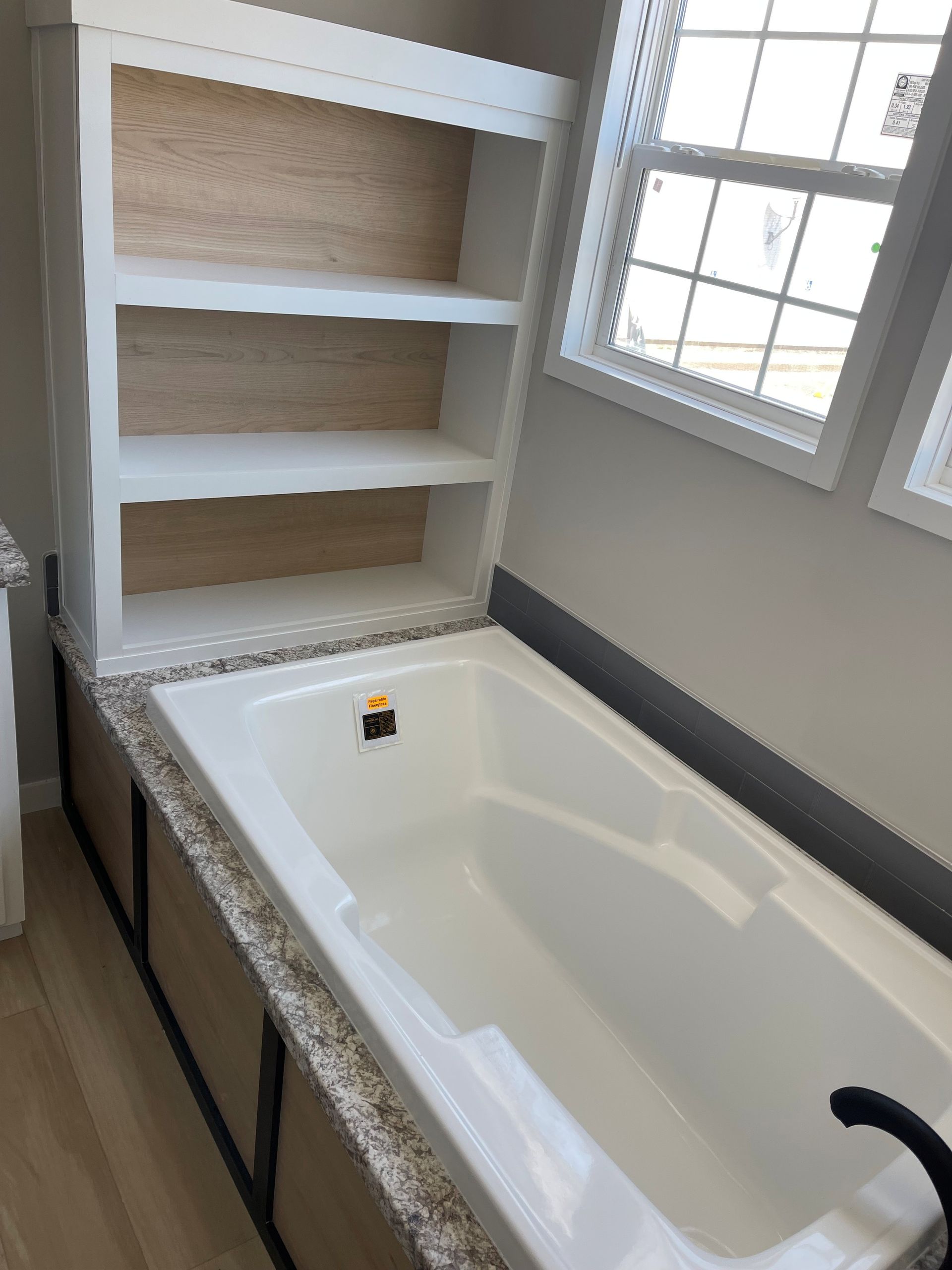 Built-in bathtub with white shelving and a window in a bright bathroom