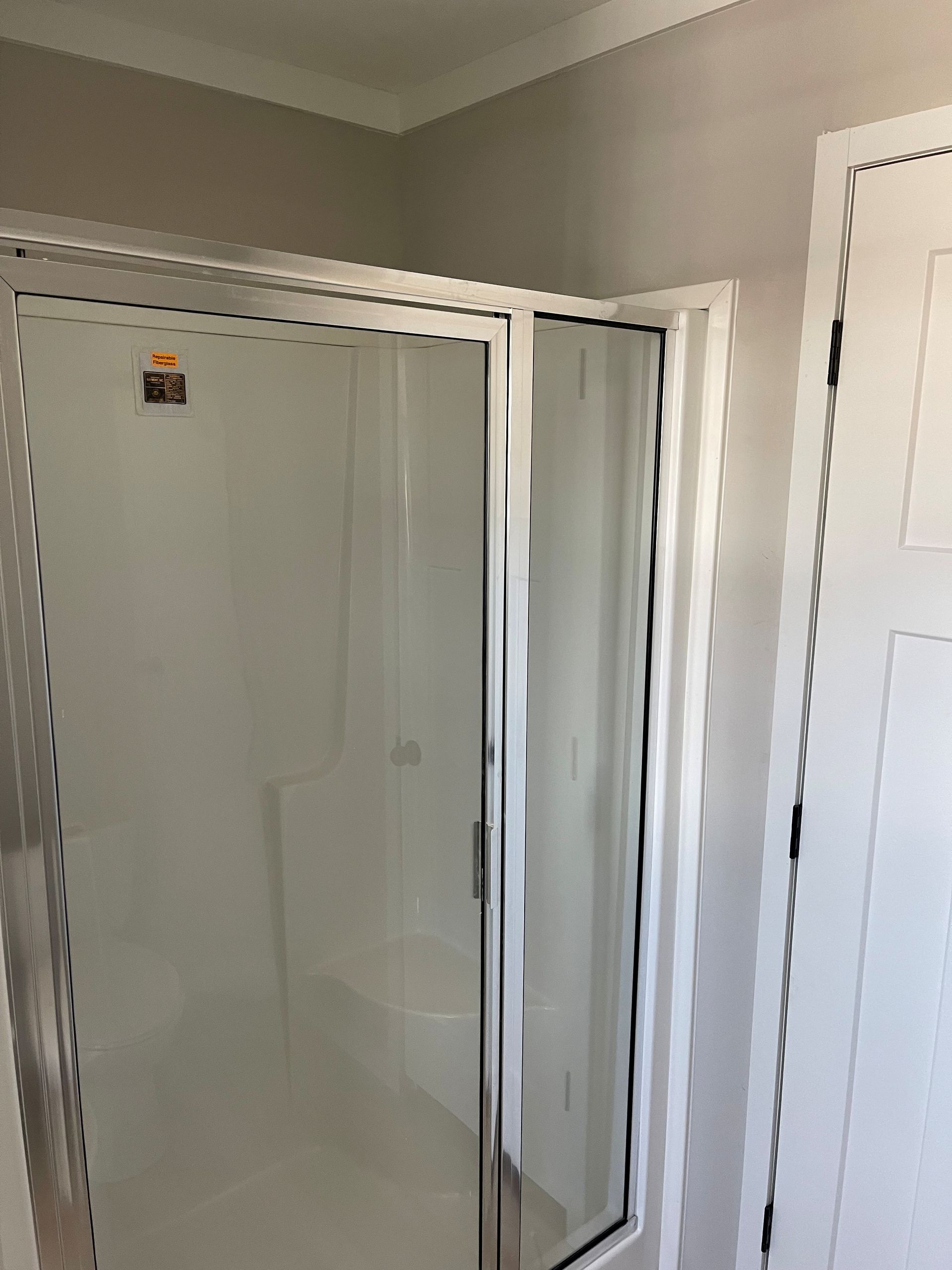 Corner shower with clear glass door in a beige bathroom