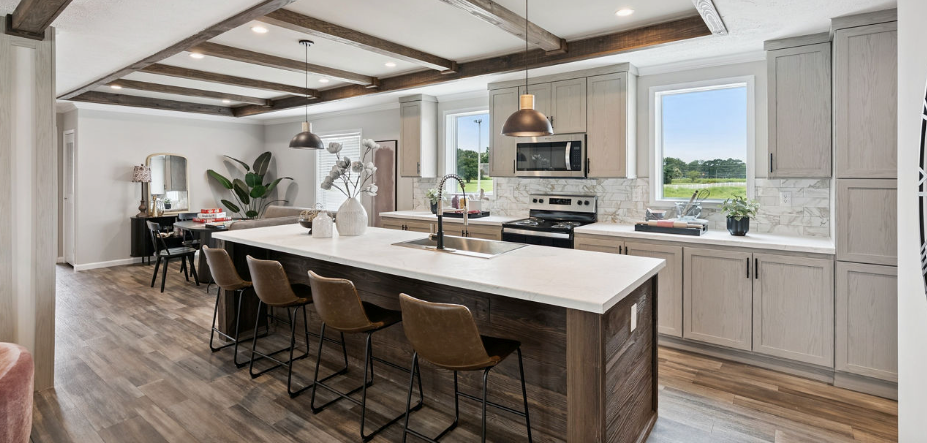 Modern kitchen with large island, wood beams, light cabinets, and dining table by the window