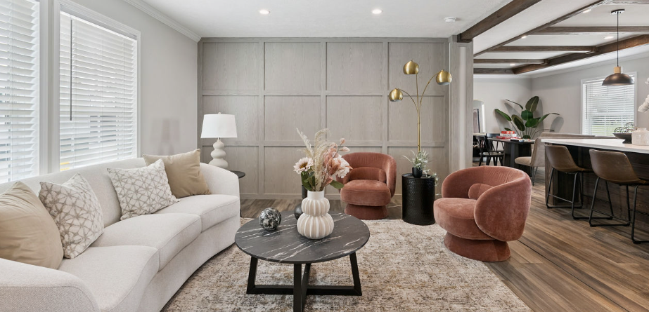 Modern open-concept living room with beige sofa, pink chairs, coffee table, and dining area by large windows