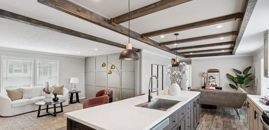 Bright open living room with white sofa, exposed beams, kitchen island, and large windows