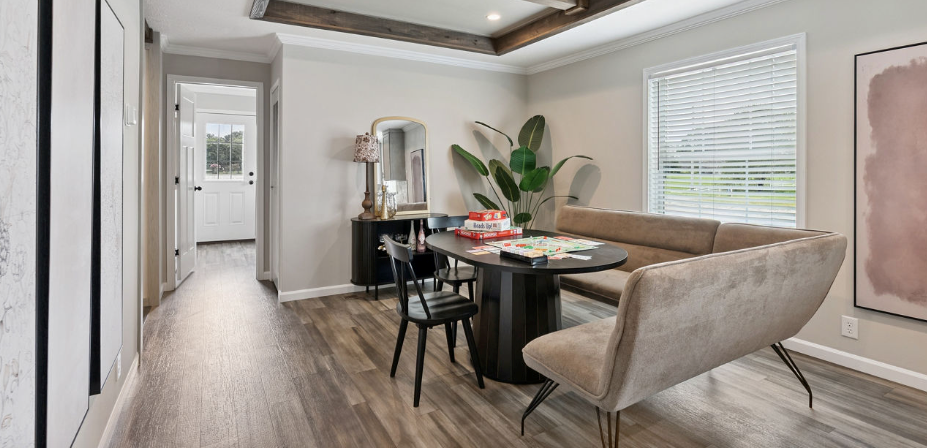 Modern dining room with a glass table, beige chairs, wall mirror, and large plant by the window