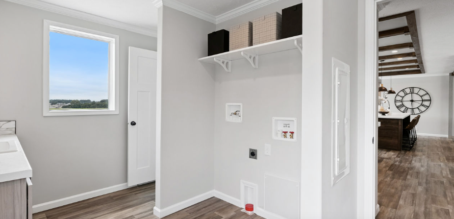 Bright hallway with white walls, built-in shelves, and a doorway to a room with stairs and a window.