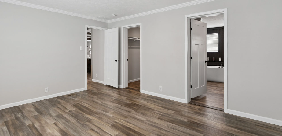 Empty modern room with gray walls, wood-look flooring, and open doors to a closet and bathroom.