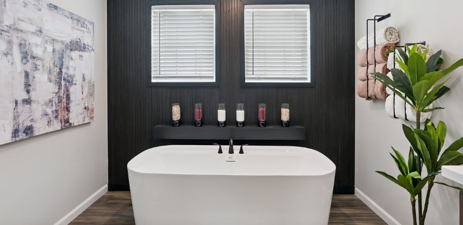 Modern bathroom with freestanding tub, black accent wall, twin windows, and green plant decor