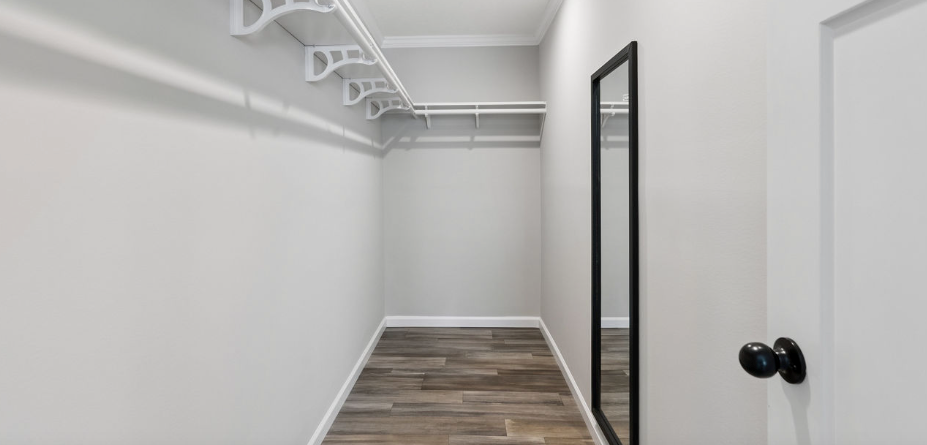 Empty white walk-in closet with wood-look floor and hanging rods on the left and back walls