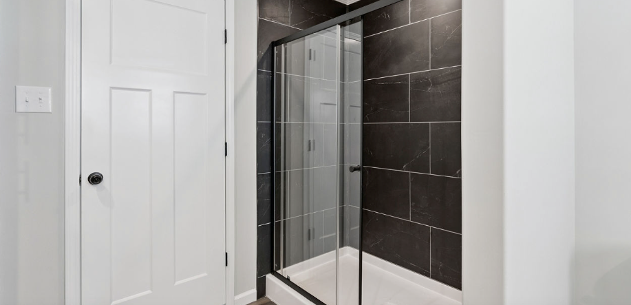 Modern bathroom with white door, glass shower enclosure, and dark tiled shower wall