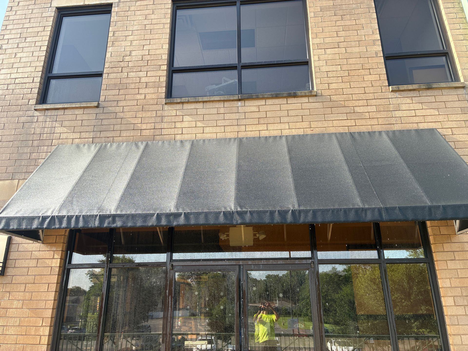Brick building storefront with black awning and large glass windows.