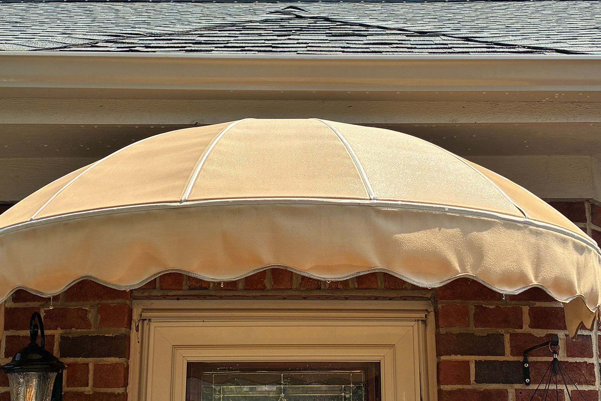 Beige scalloped window awning above a brick house window under gray siding