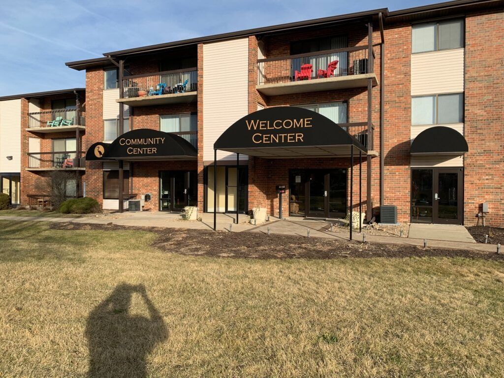 Apartment building with brick balconies and a black awning labeled “WELCOME CENTER”
