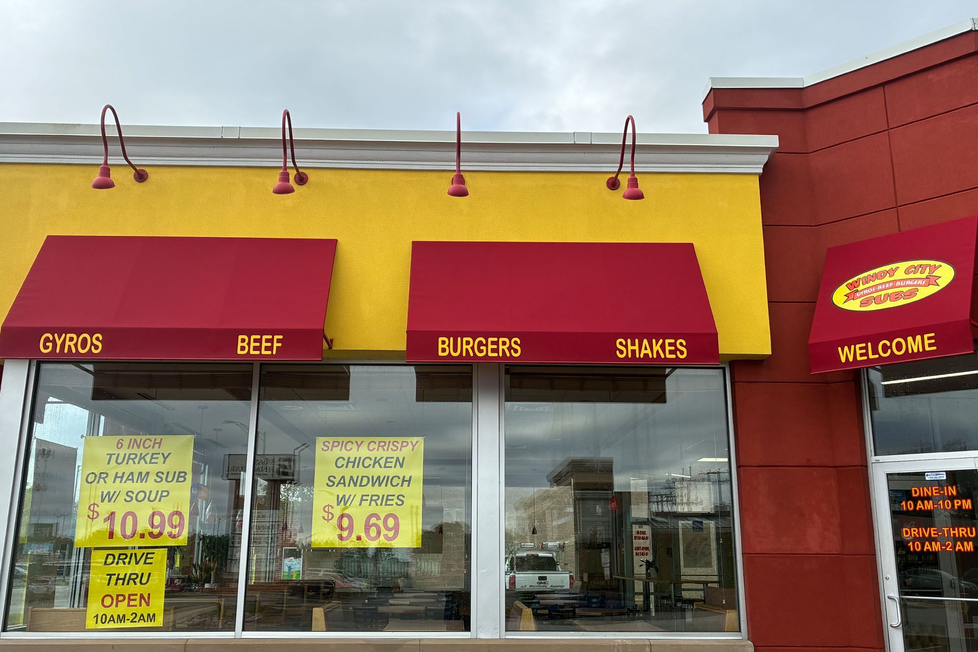Fast-food storefront with red-and-yellow awnings and signs for gyros, beef, burgers, shakes, and welcome.