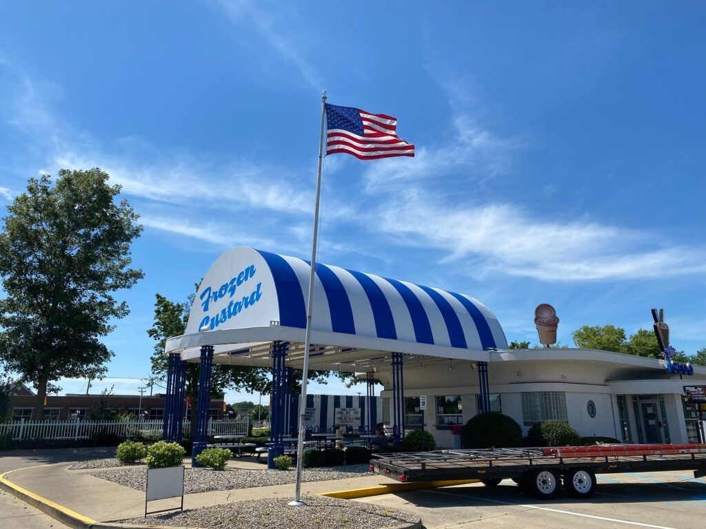 Entrance with blue-and-white striped canopy and American flag under a clear sky