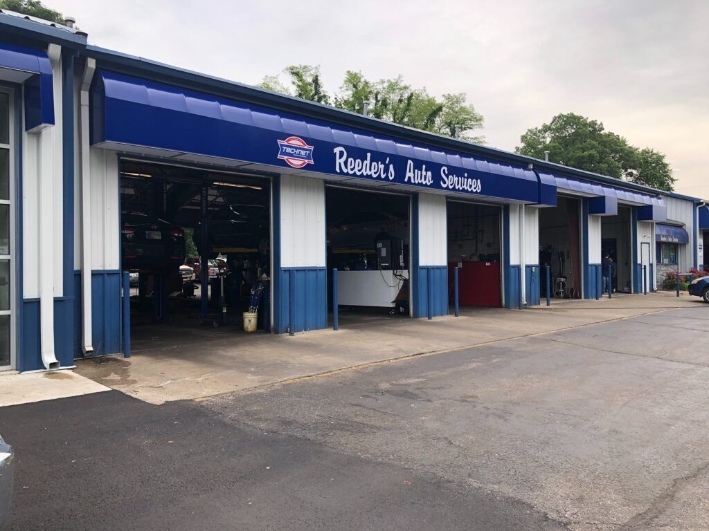 Blue and white auto repair garage with open bays and a paved lot in front