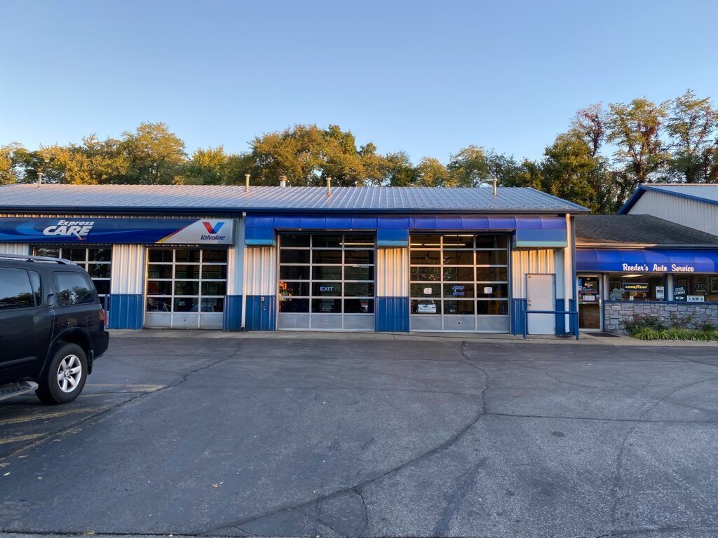 Blue-roofed auto service building with garage bays and a parked black truck in front