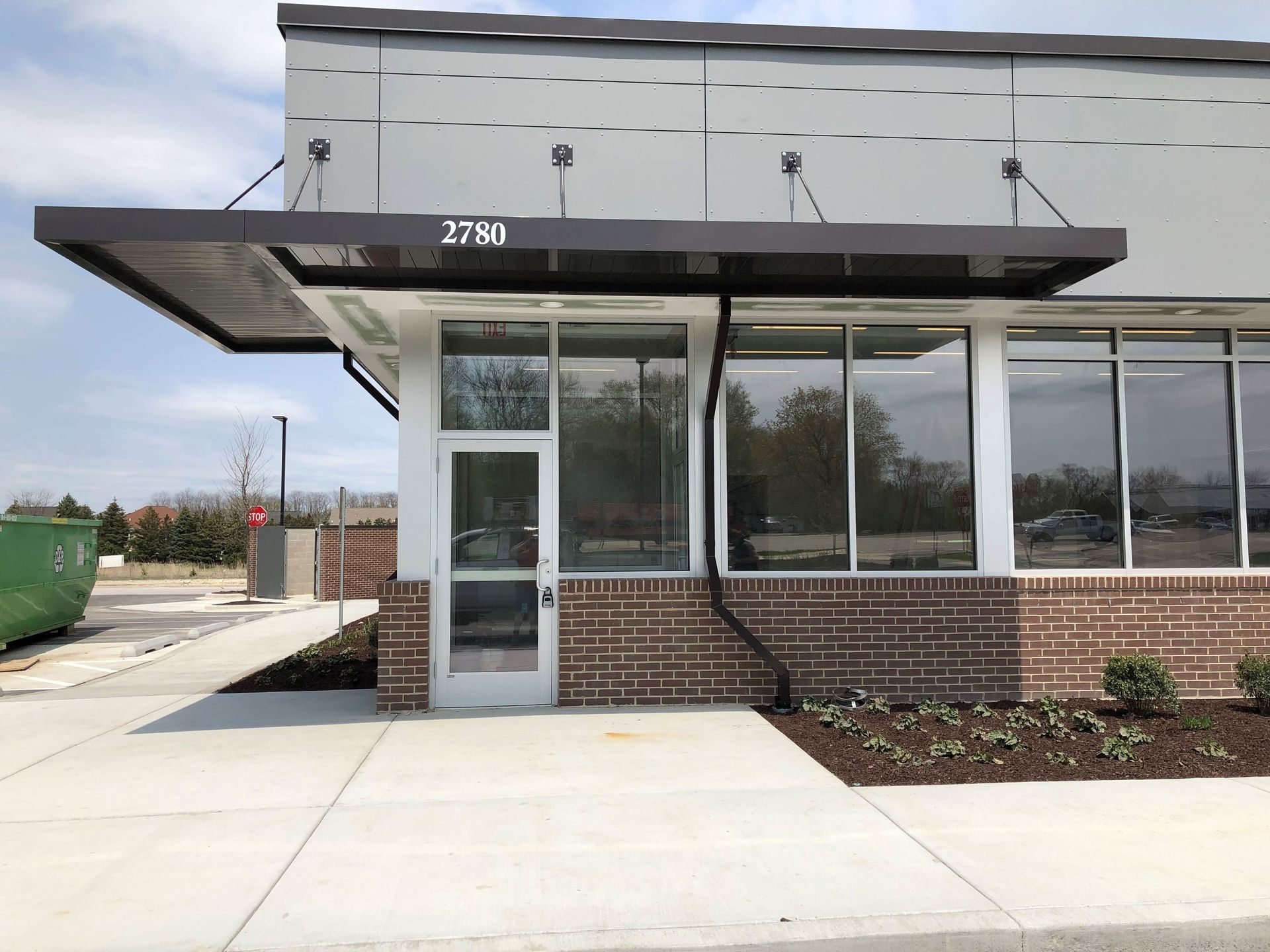 Storefront entrance with brick base, large windows, and black awning on a sunny sidewalk